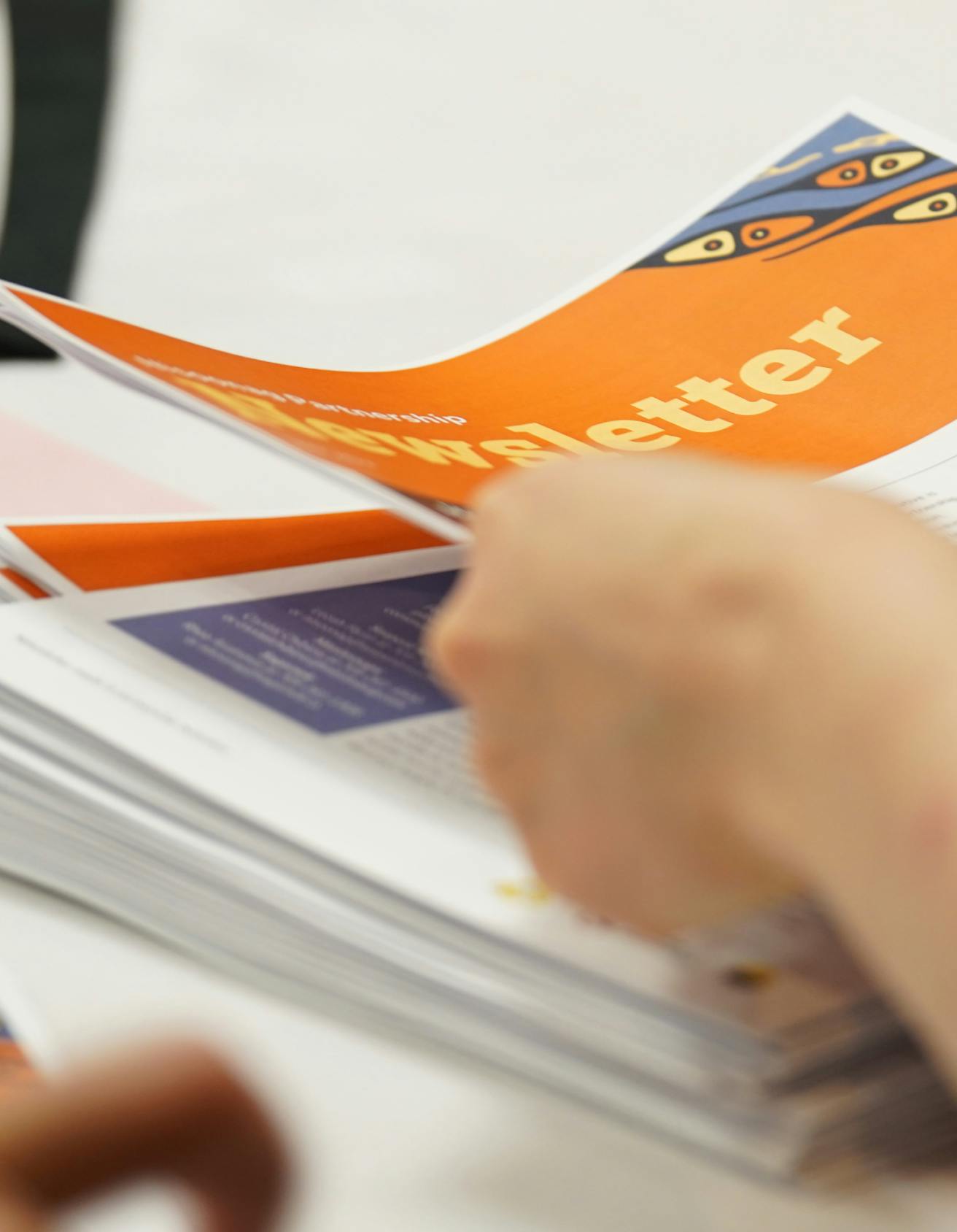 Close up of a hand placing a newsletter on top of a pile of newsletters