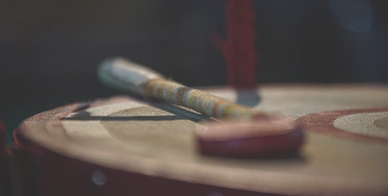 A customary drum stick lays on top of a drum in a dimly lit room