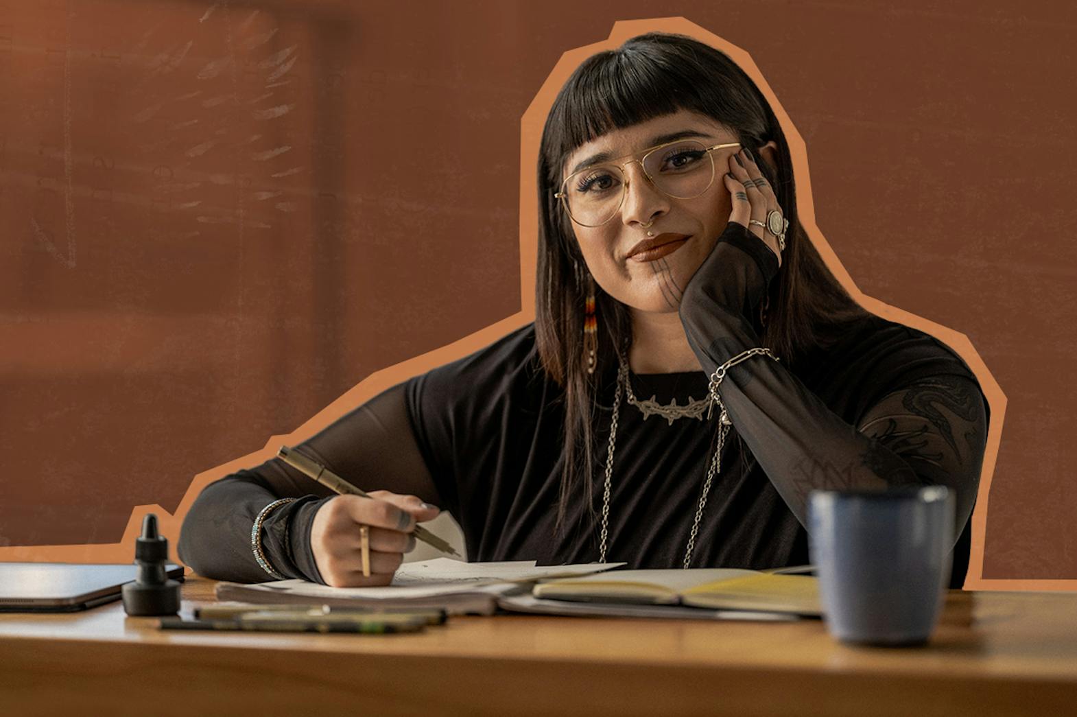 A non-binary Indigenous artist sitting at a desk drawing