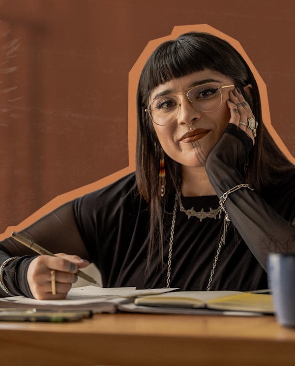 A non-binary Indigenous artist sitting at a desk drawing