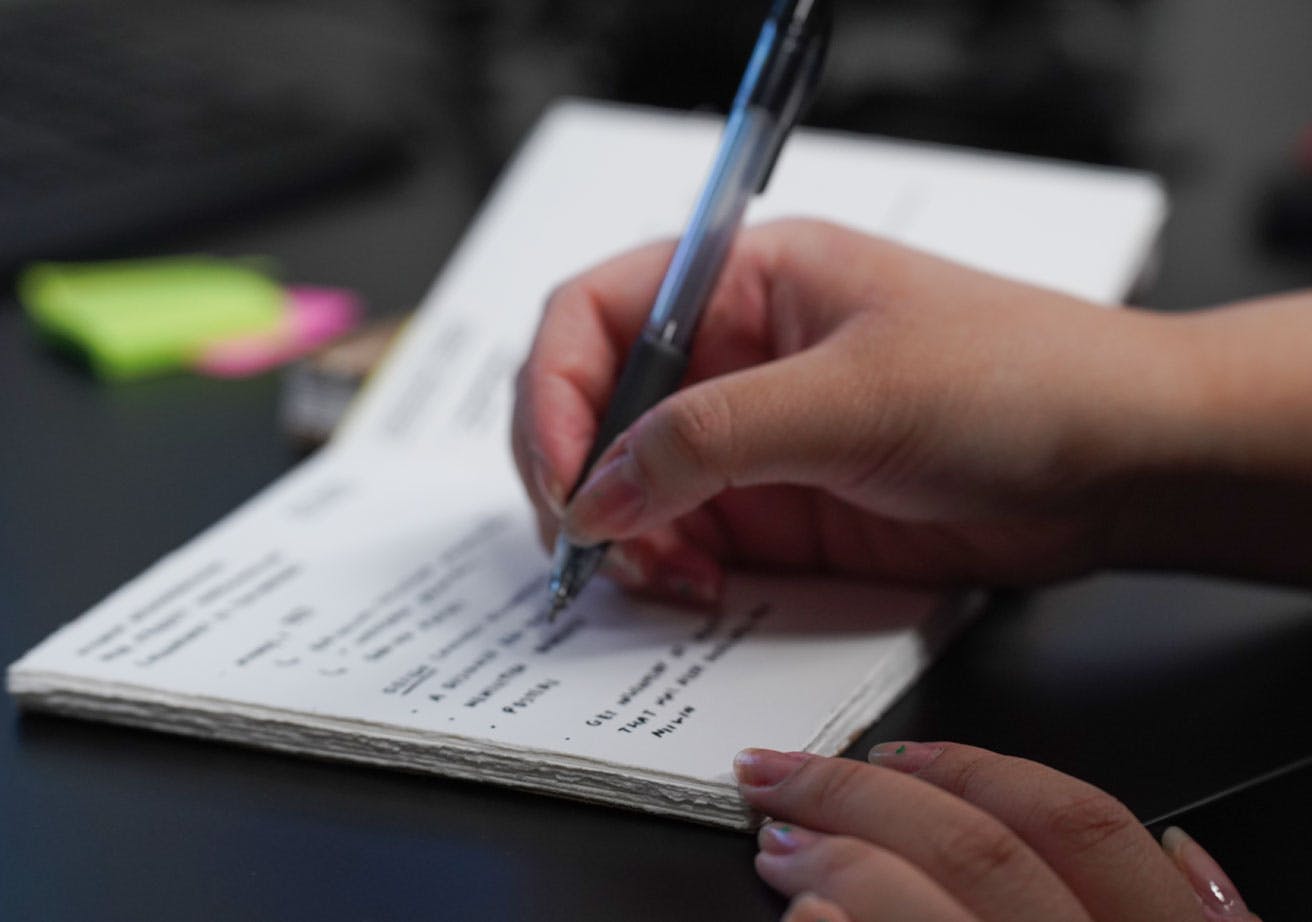 Close up of a hand writing in a notebook on a desk