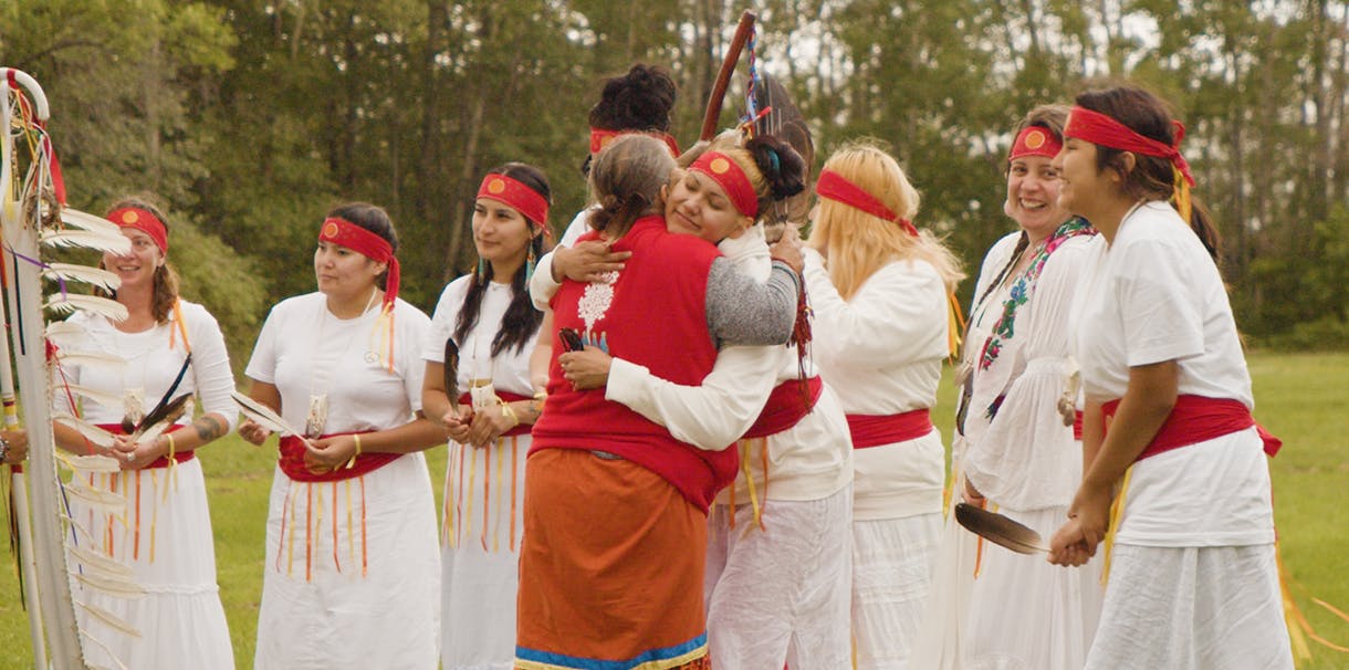 A group of Indigenous women hugging and wearing customary Indigenous regalia.