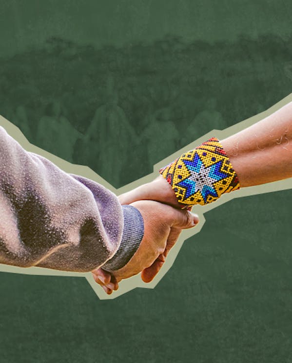 Two people hold hands. One wears a gray long-sleeve shirt, the other wears a colorful beaded bracelet against a green background.