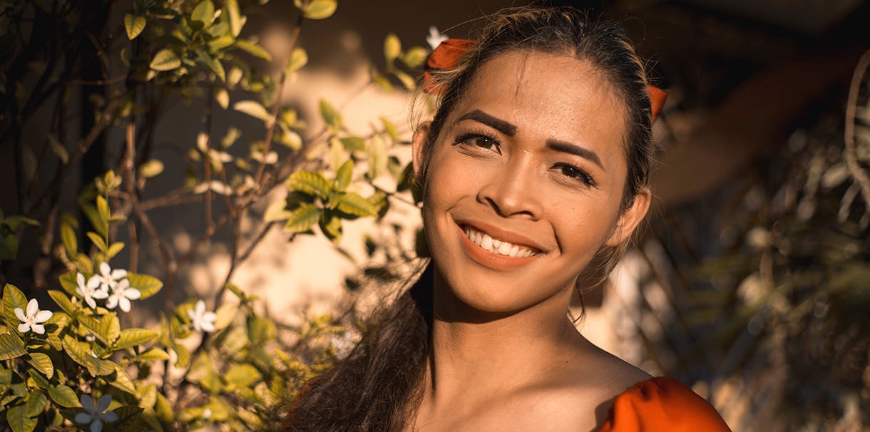 A Filipino woman in an orange dress smiles warmly at the camera.