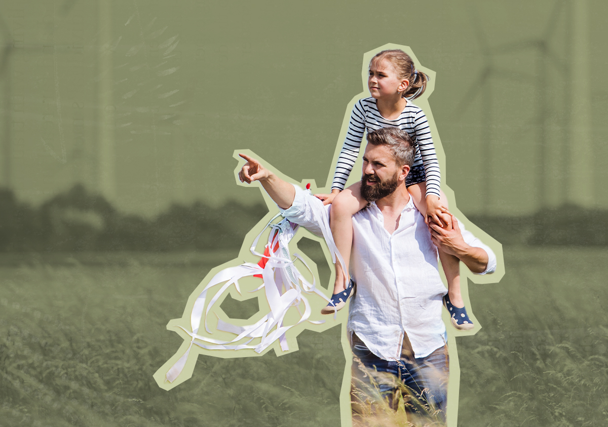 A man pointing into the distance with a child on his shoulders, standing in front of several large wind turbines against a clear blue sky.