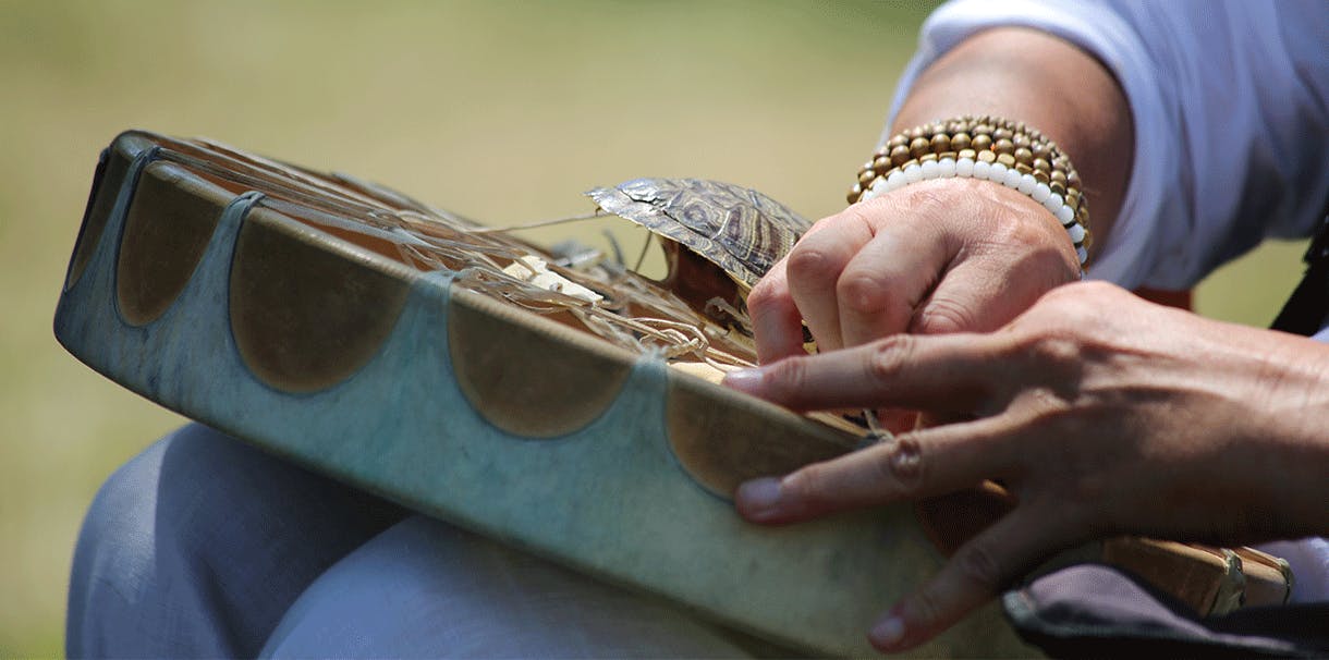 Hands adjusting the strings on the back of a ceremonial drum