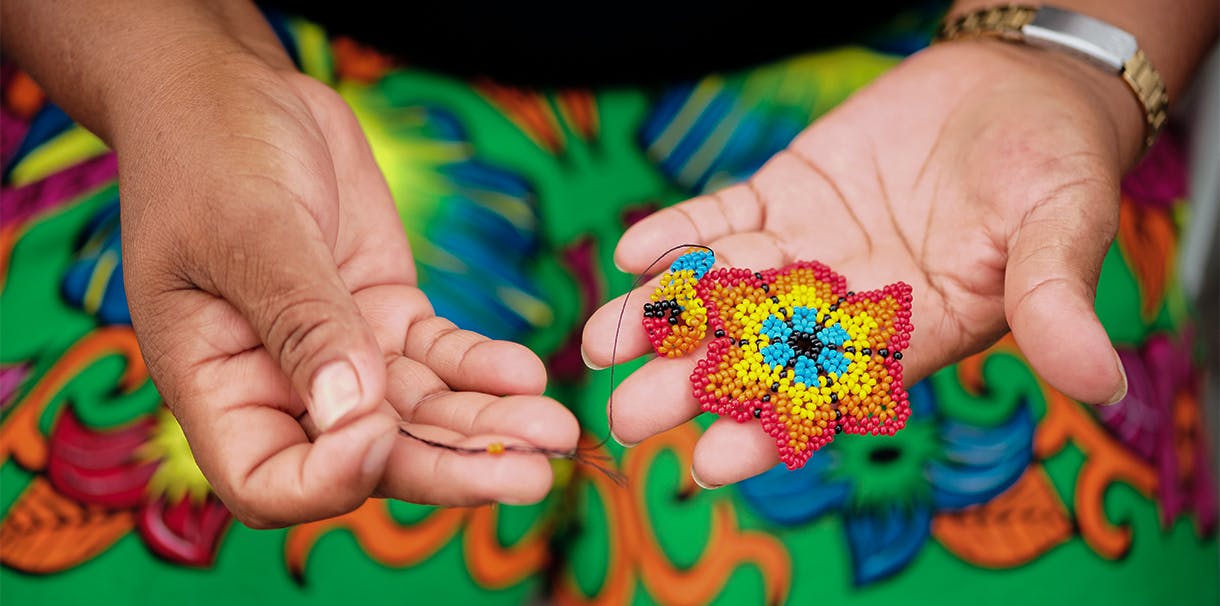 An Indigenous women wearing a bead skirt, holds a beaded flower in her hands