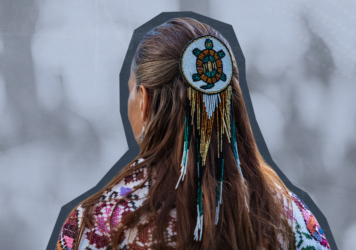 The back of an Indigenous woman's head with a beaded turtle medallion in her hair