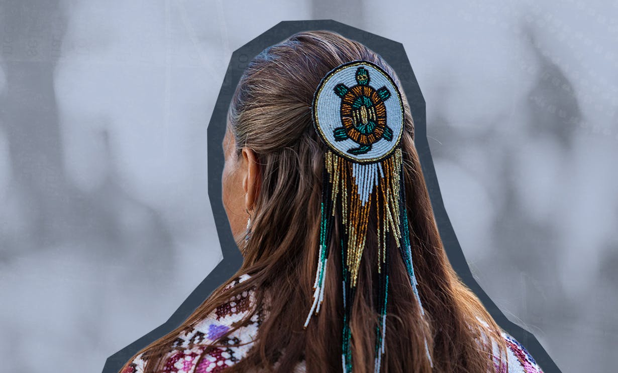 The back of an Indigenous woman's head with a beaded turtle medallion in her hair