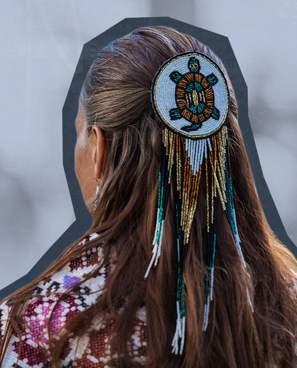 The back of an Indigenous woman's head with a beaded turtle medallion in her hair