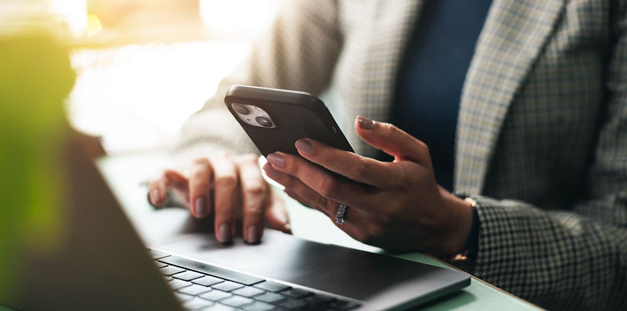 A person holds a phone with their hand resting on a laptop