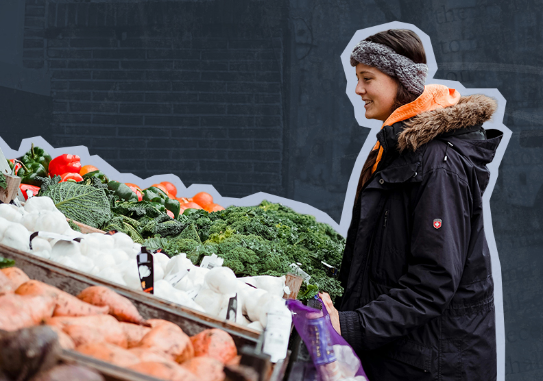 A woman stands outside looking at a variety of fresh produce at a farmers market