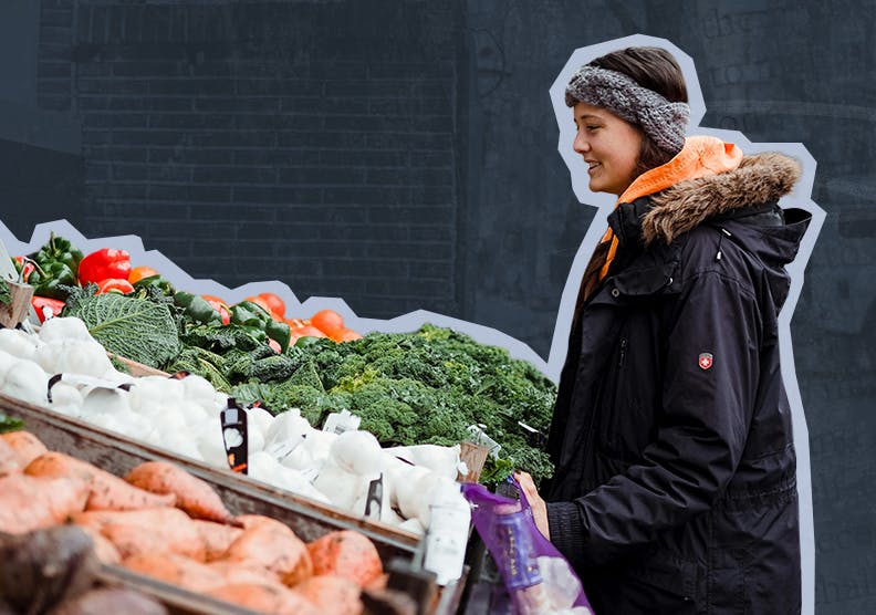 A woman stands outside looking at a variety of fresh produce at a farmers market