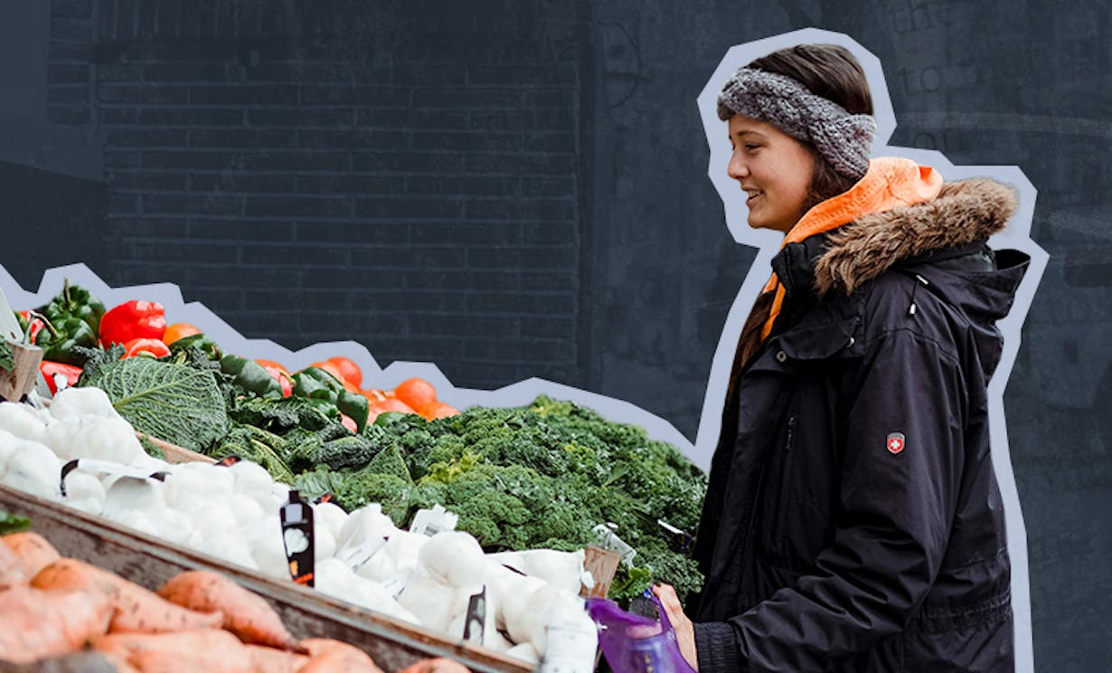 A woman stands outside looking at a variety of fresh produce at a farmers market