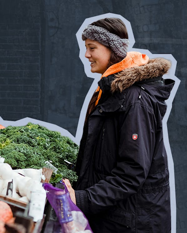 A woman stands outside looking at a variety of fresh produce at a farmers market