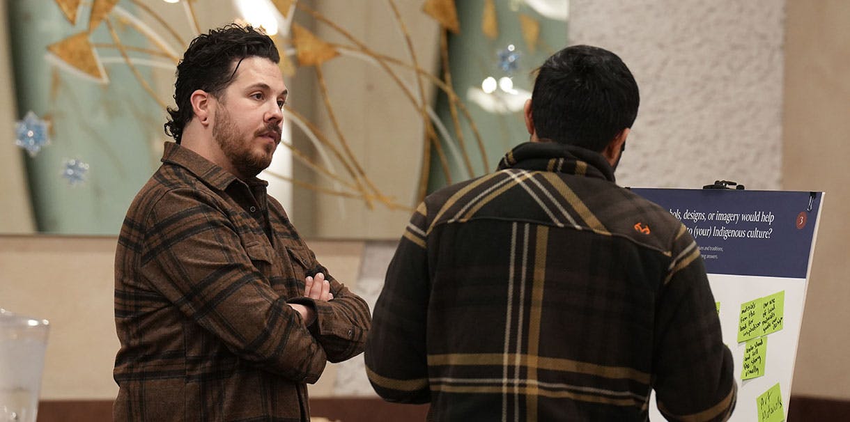 Two men conversing in front of a board filled with sticky notes