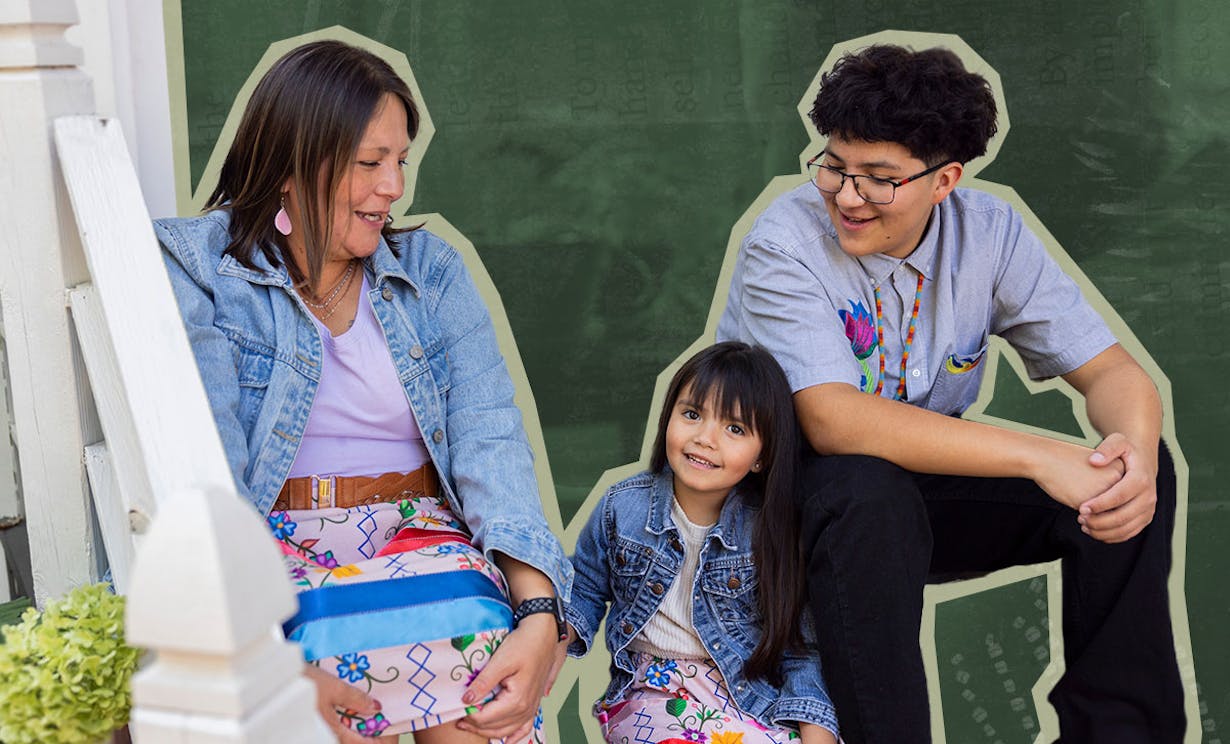 An Indigenous family sits on a porch smiling at each other. The women are wearing colourful ribbon skirts.