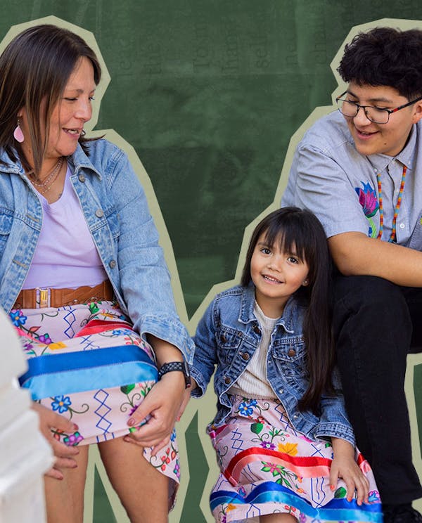 An Indigenous family sits on a porch smiling at each other. The women are wearing colourful ribbon skirts.