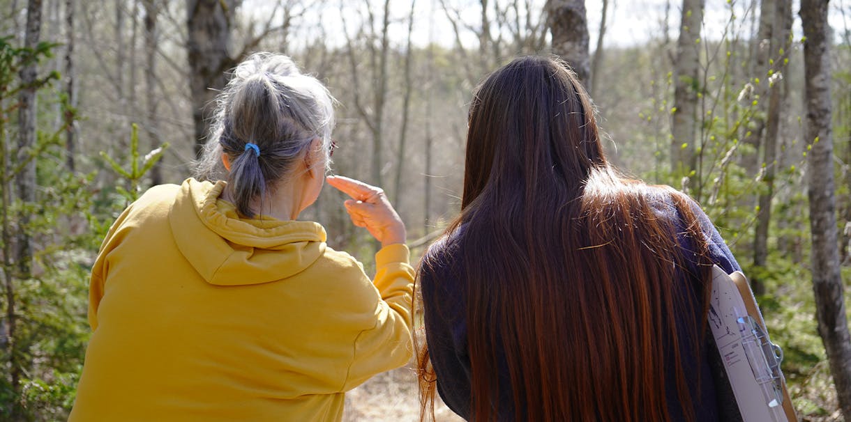 Eden Klein leans in close with an Elder, looking into a forest
