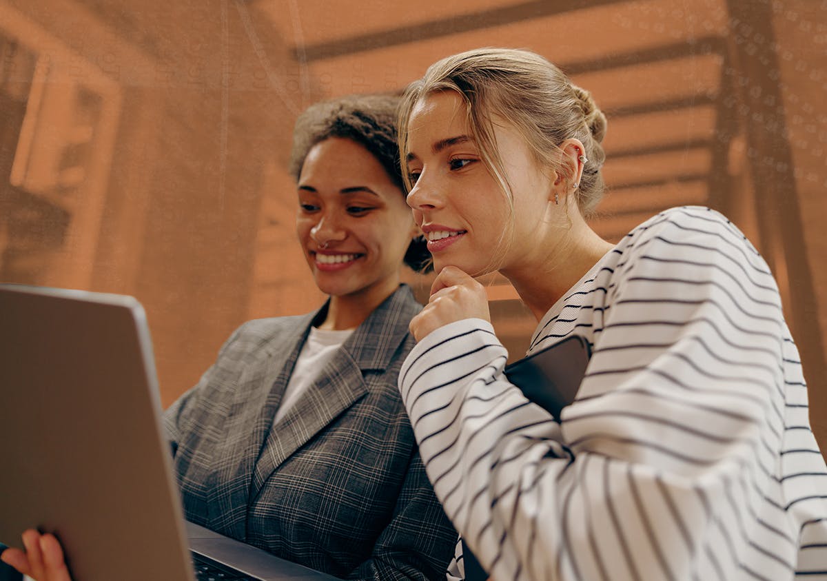 Two women lean close together looking at a computer screen