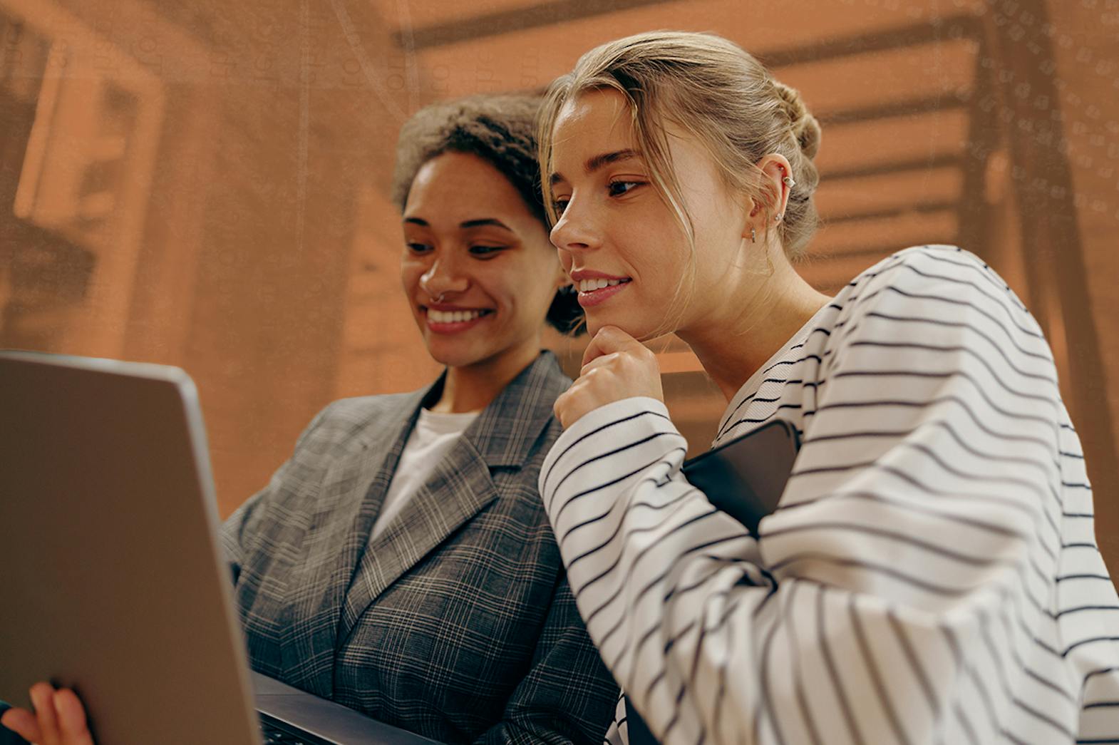 Two women lean close together looking at a computer screen