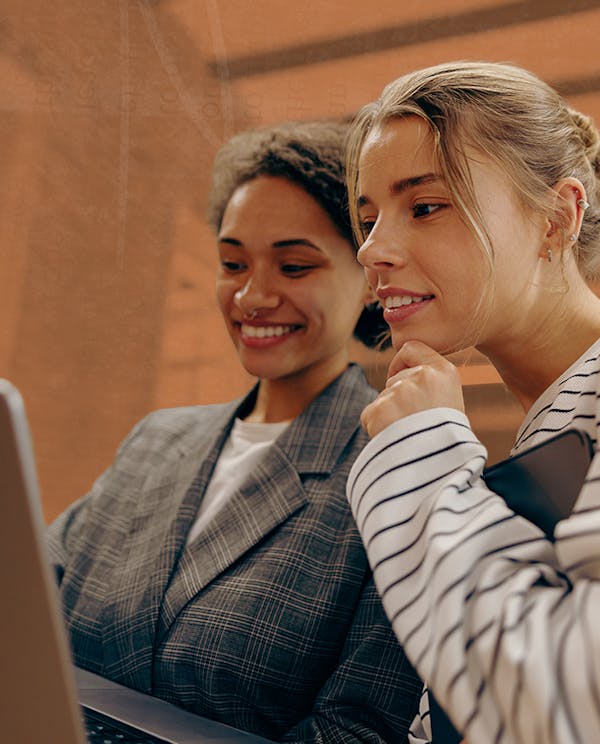 Two women lean close together looking at a computer screen