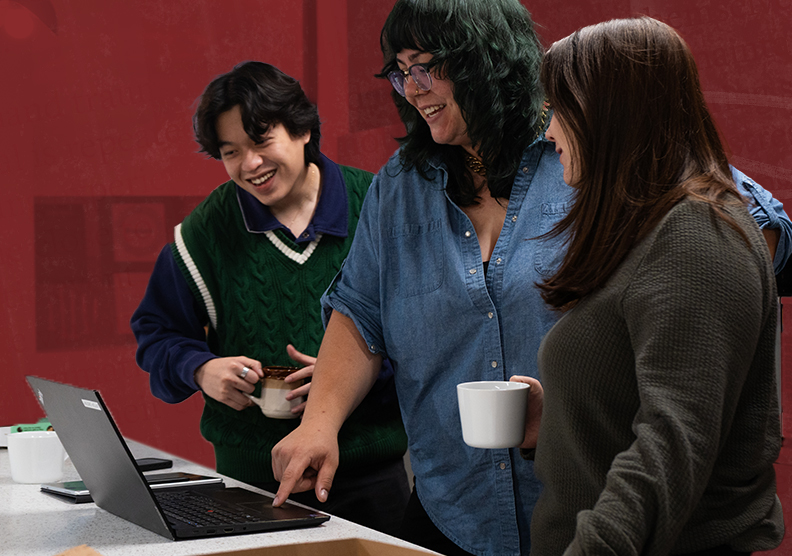 Staff at Narratives huddle around a computer smiling and conversing