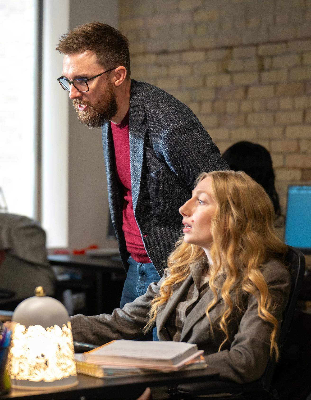 Man in glasses in discussion with a colleague at her desk
