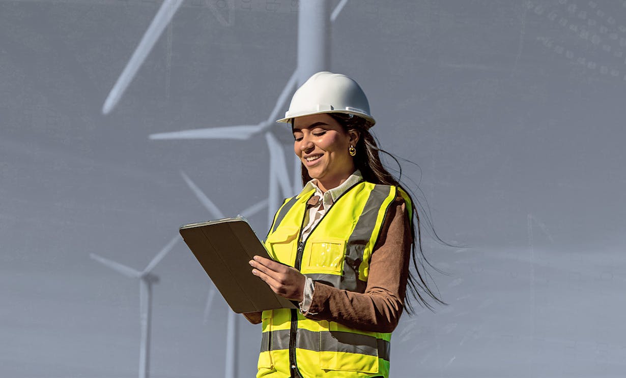 A women in a safety vest holding a clipboard standing in front of windmills