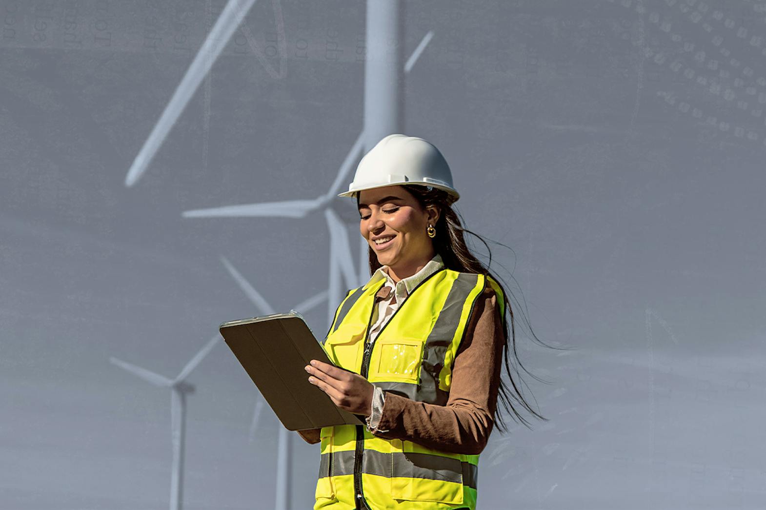 A women in a safety vest holding a clipboard standing in front of windmills