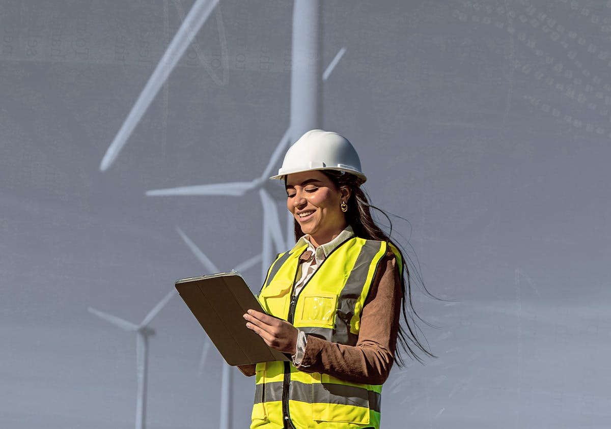 A women in a safety vest holding a clipboard standing in front of windmills