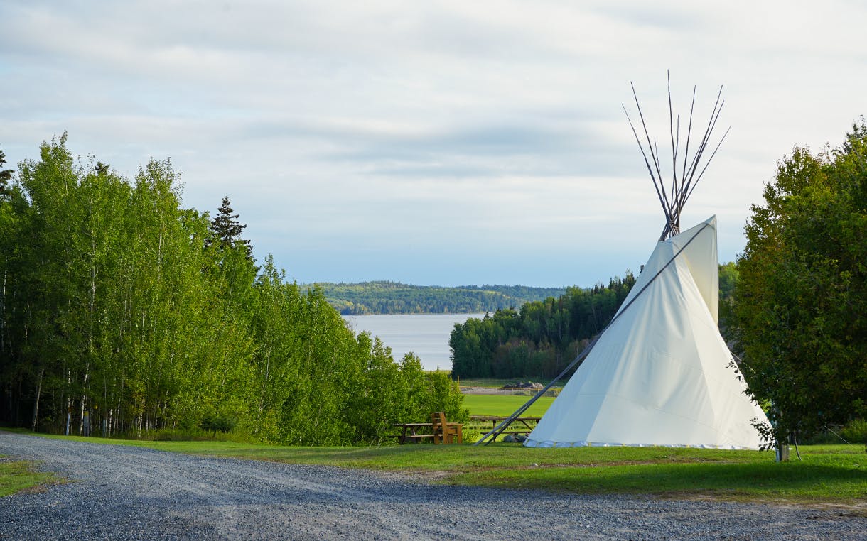 A scenic landscape in Kenora, Ontatio. A tipi and firepit sit in front of a lake.