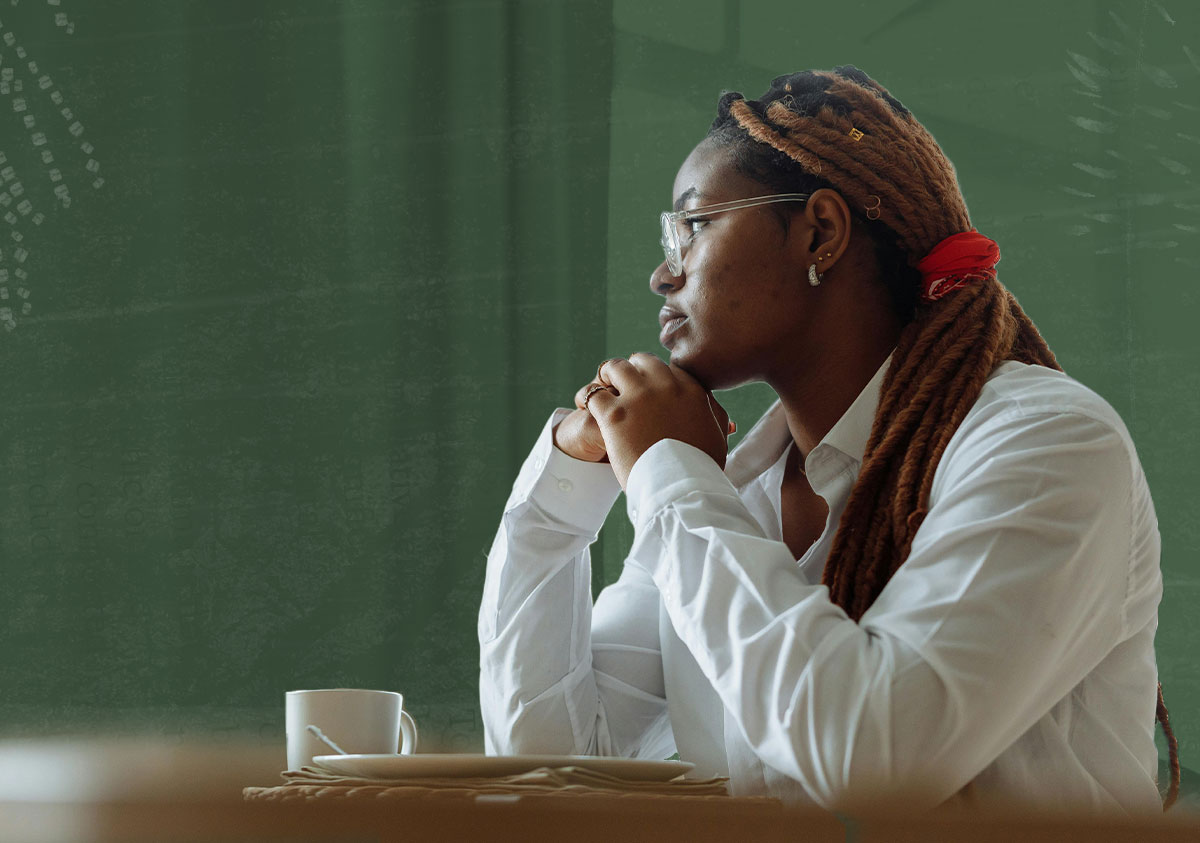 A women sits at a table in a white shirt and stares out a window
