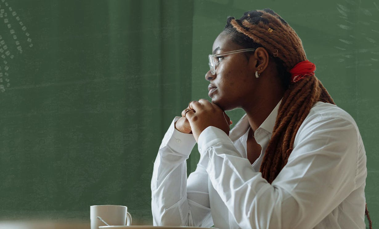 A women sits at a table in a white shirt and stares out a window