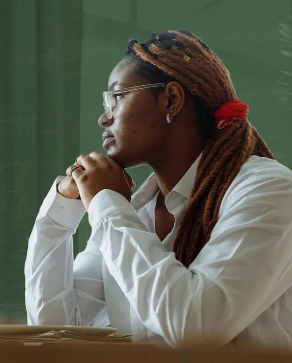 A women sits at a table in a white shirt and stares out a window