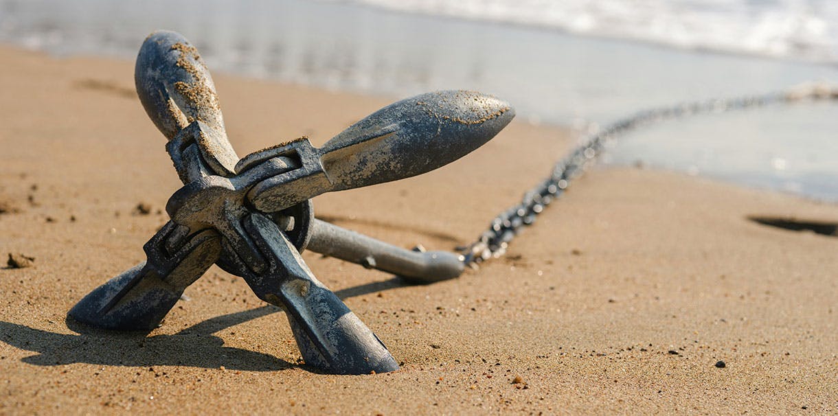 An anchor attached to a chain laying in the sand close to shore