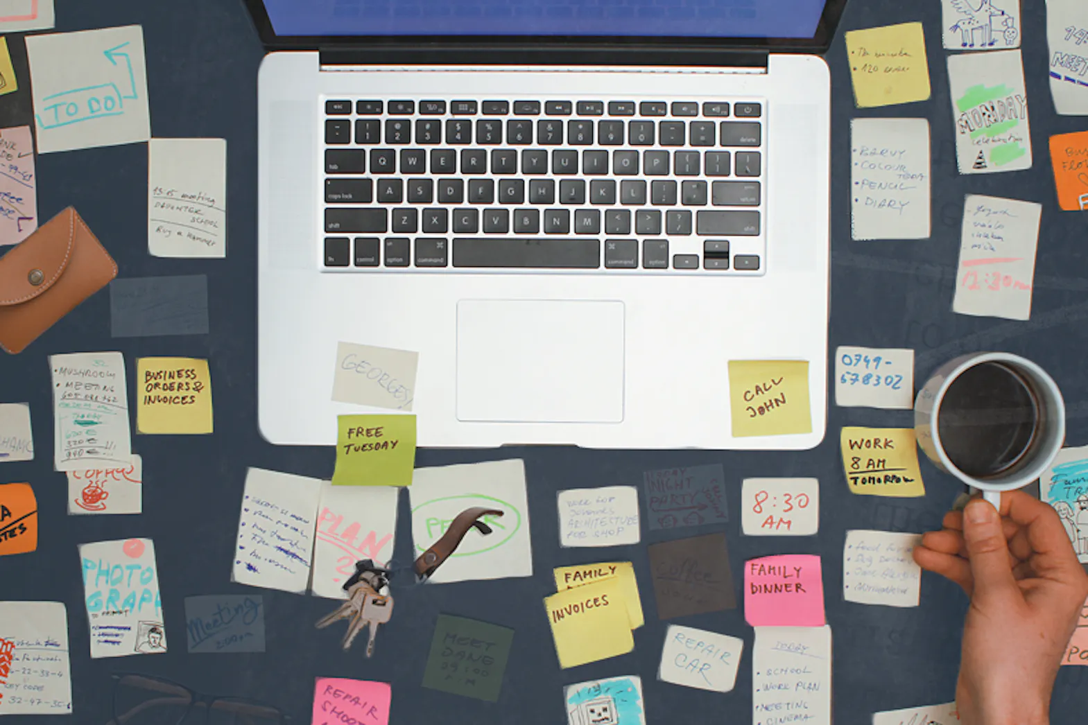 An overhead view of a desk with a computer open. The desk is filled with sticky notes and other objects showing reality of remote work.