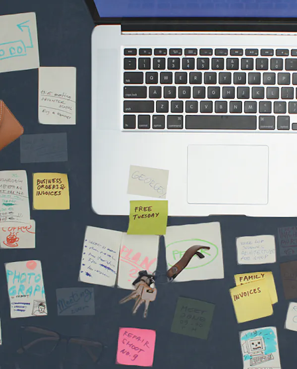 An overhead view of a desk with a computer open. The desk is filled with sticky notes and other objects showing reality of remote work.