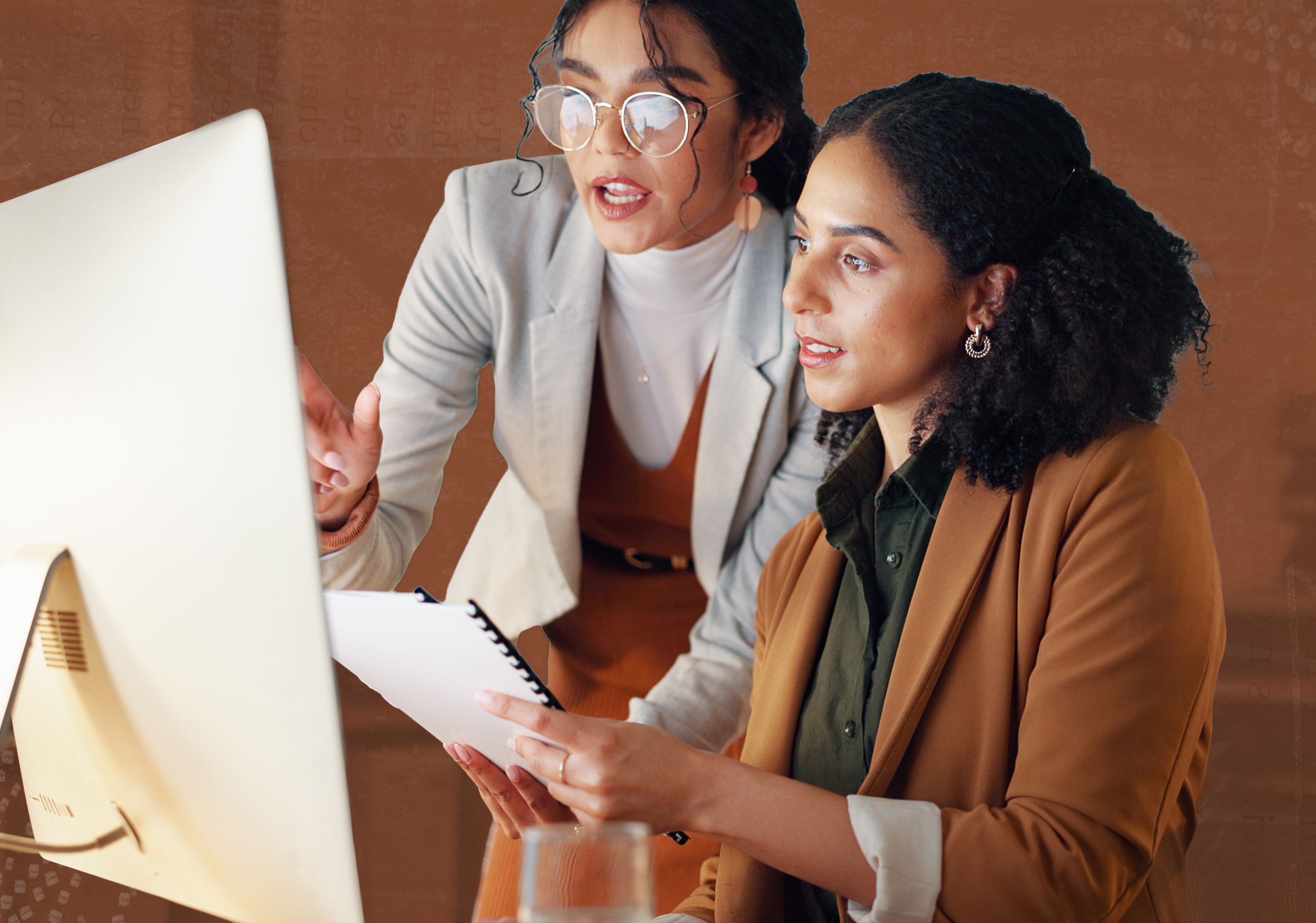 Two women look a ta computer in an office setting