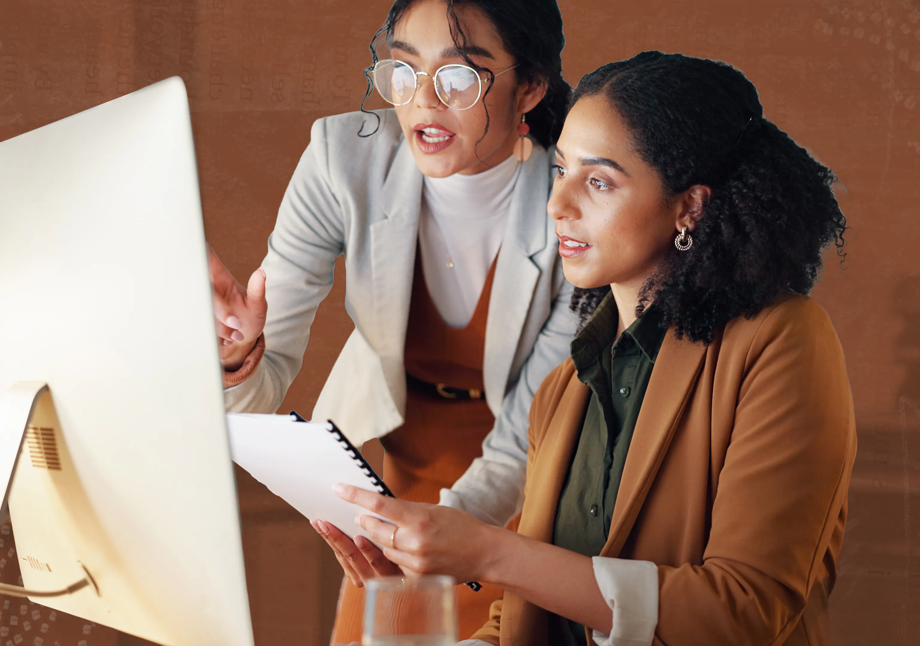 Two women look at a computer in an office setting
