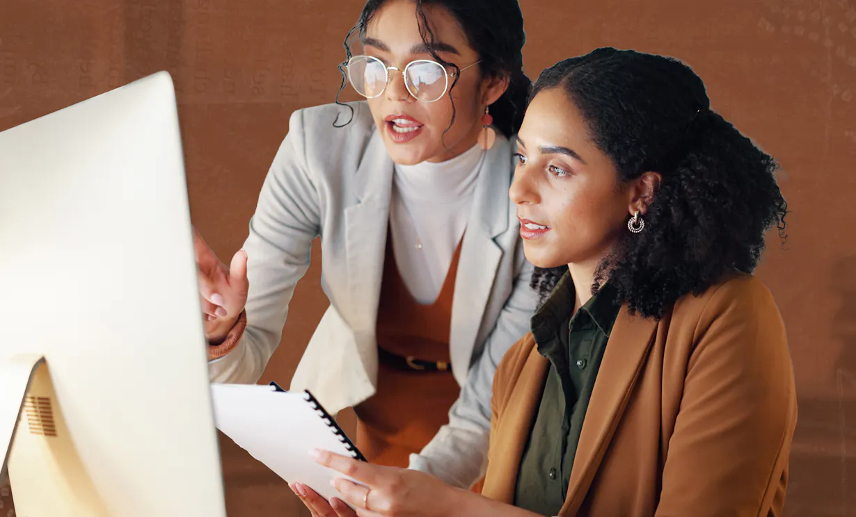 Two women look a ta computer in an office setting