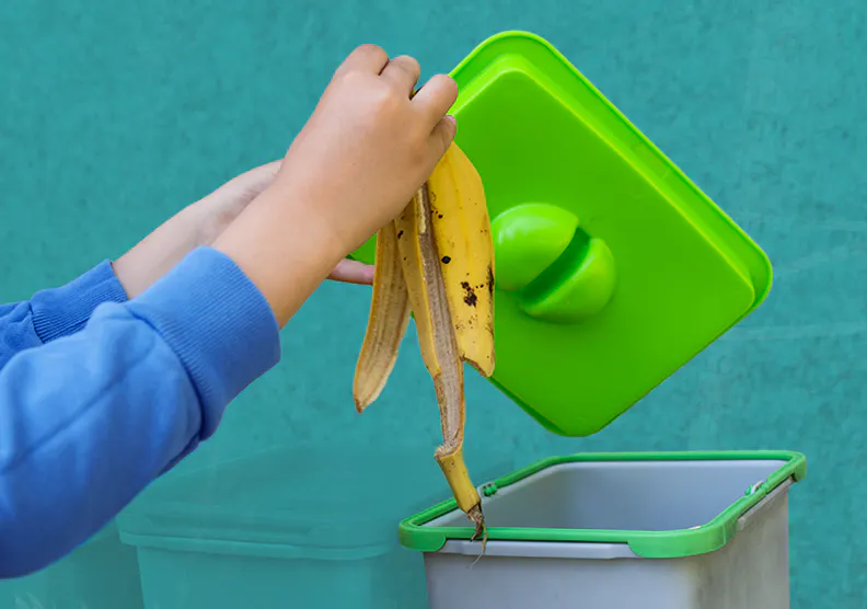 A hand placing a banana peel into an indoor compost bin
