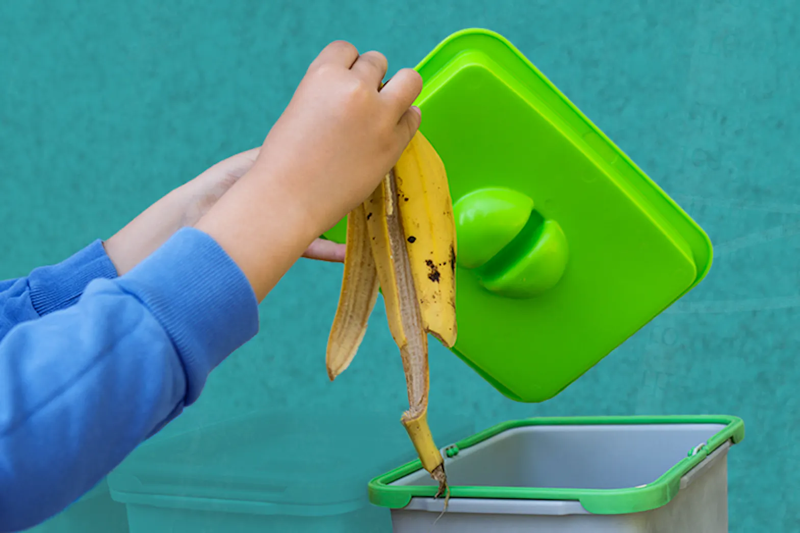 A hand placing a banana peel into an indoor compost bin
