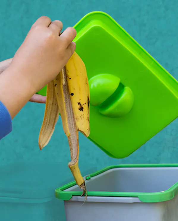 A hand placing a banana peel into an indoor compost bin