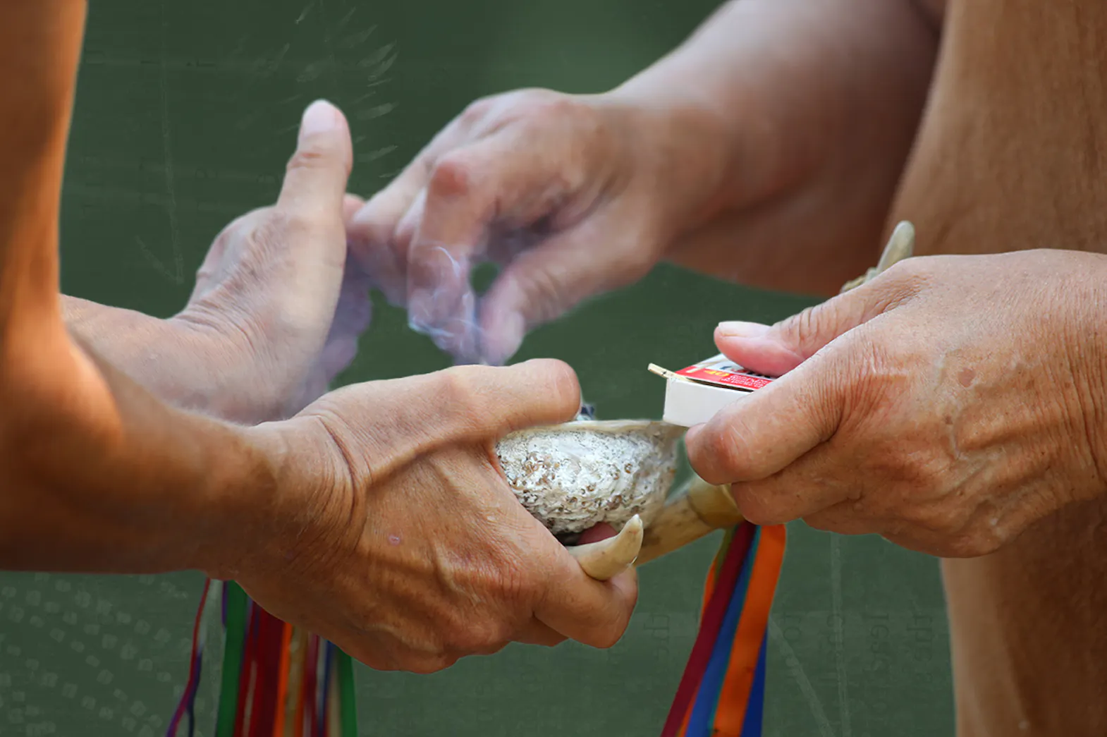 A person holding out their hands holding a shell with sage in it. The other holds a box of matches and lights the sage to perform a ceremonial smudge.