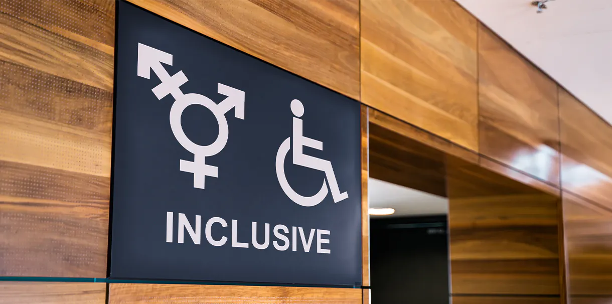 Gender inclusive washroom signage hanging on wooden wall
