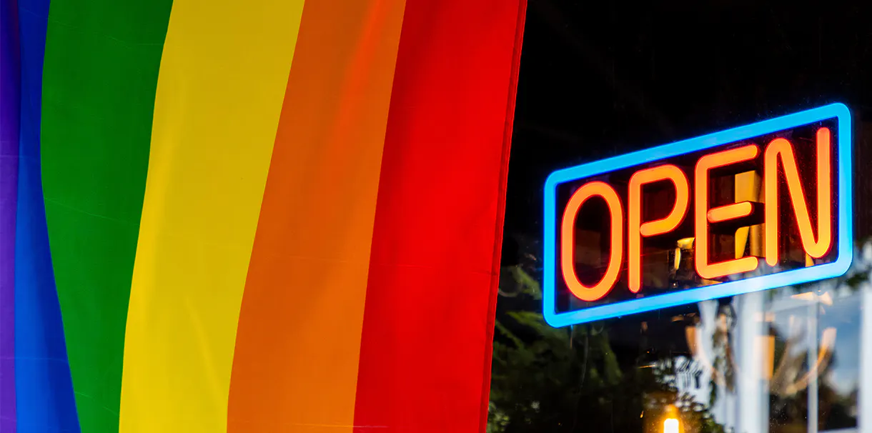 A business window displays a pride flag. The window has a sign that reads 'Open'