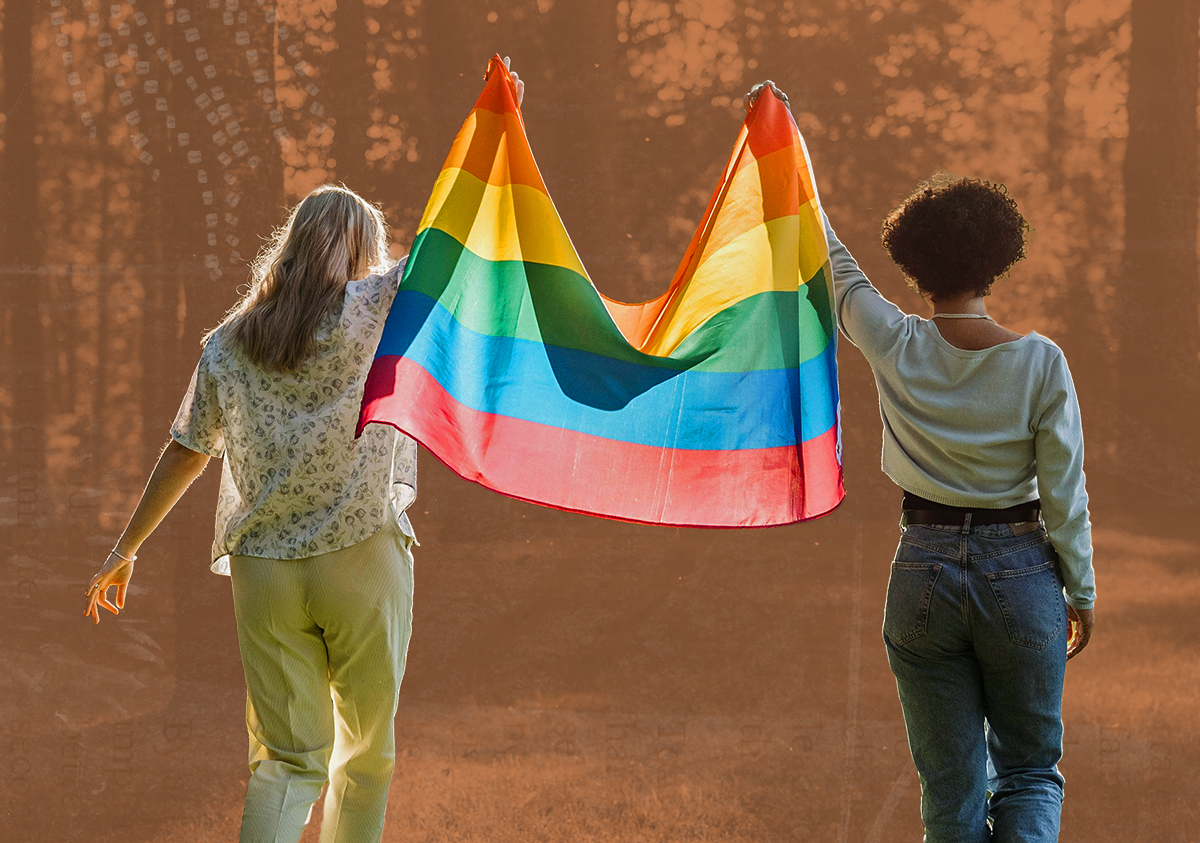 Two people hold a pride flag above their heads walking in nature