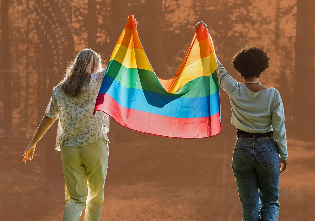 Two people hold a pride flag above their heads walking in nature