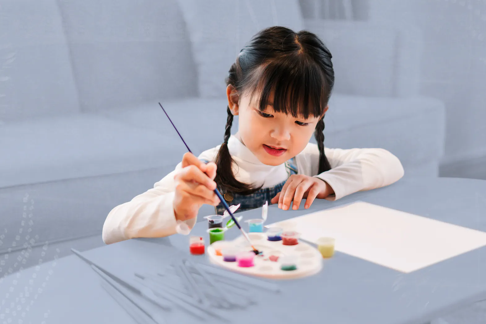 A small child sits at a coffee table painting on a piece of paper.